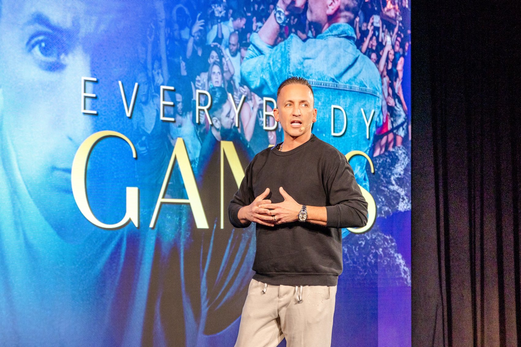 Clinton Sparks speaking on stage in front of an Everybody Games screen
